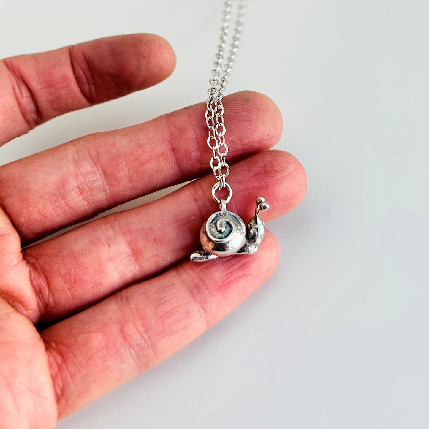 Silver snail pendant necklace held in a hand against a light background