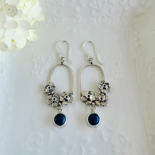 Silver earrings with floral designs and blue stones on a white textured background