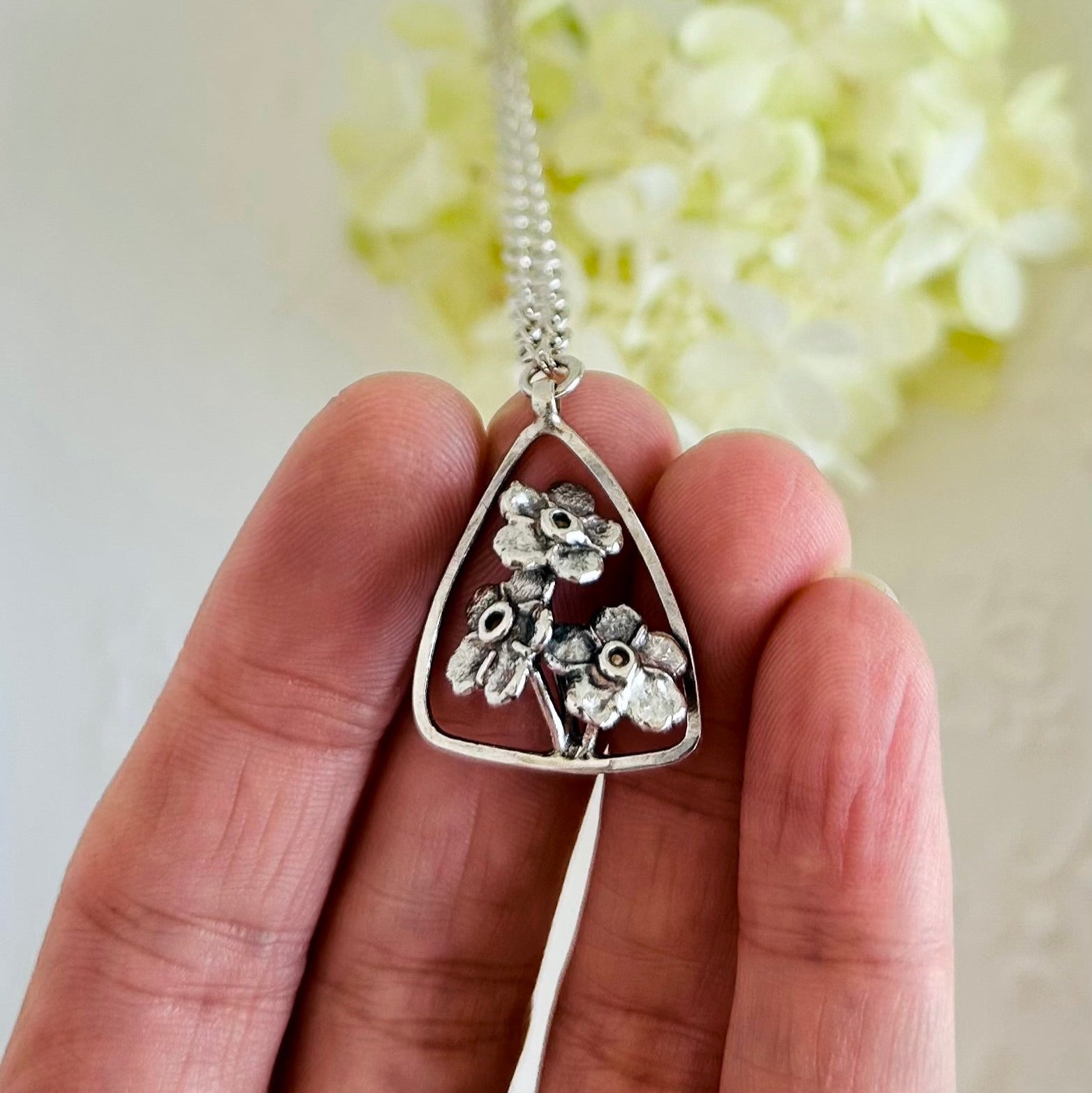 Silver floral pendant necklace held by a hand with a light background