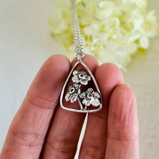 Silver floral pendant necklace held by a hand with a light background