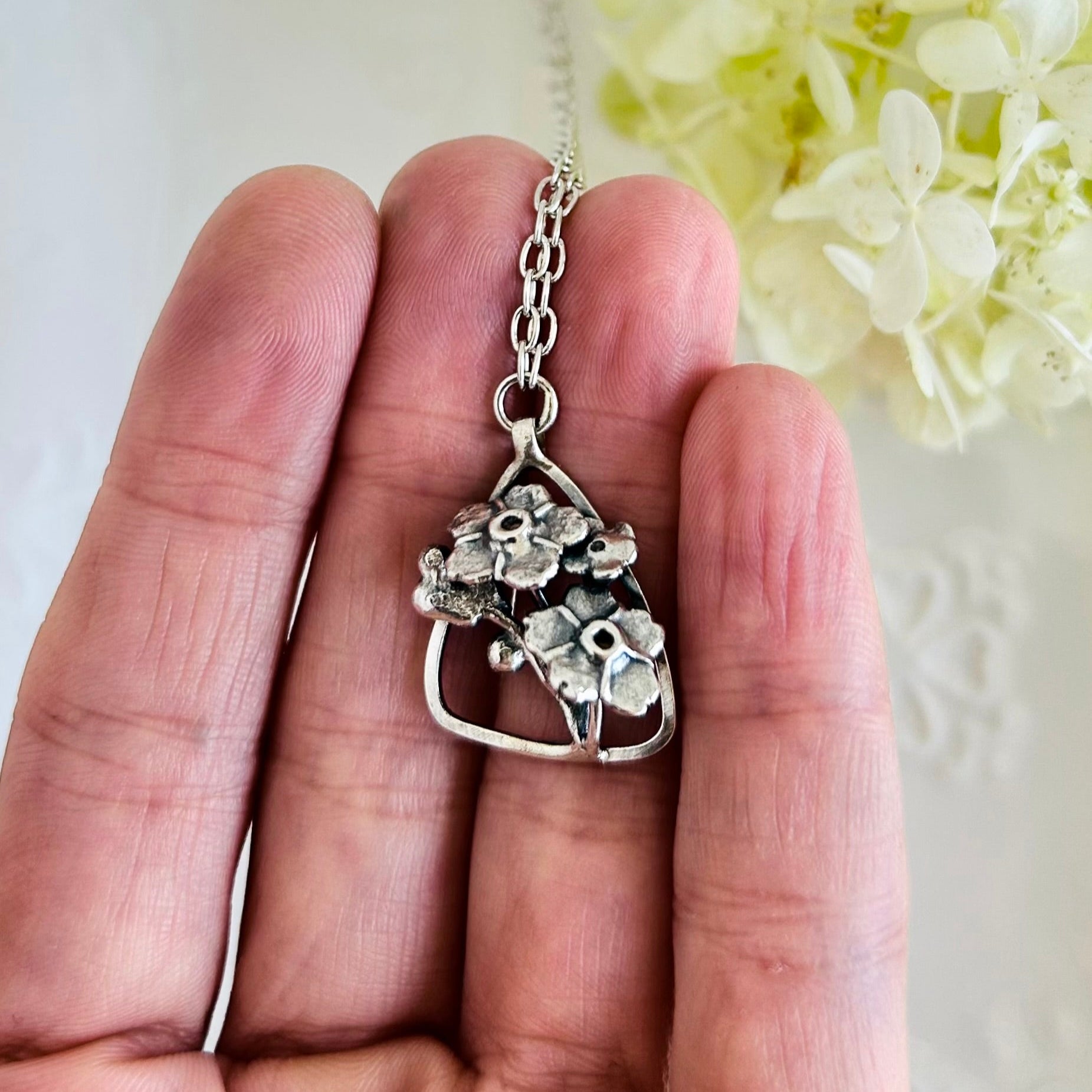 Silver necklace with a floral pendant held between fingers against a light background