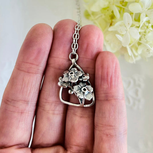 Silver necklace with a floral pendant held between fingers against a light background