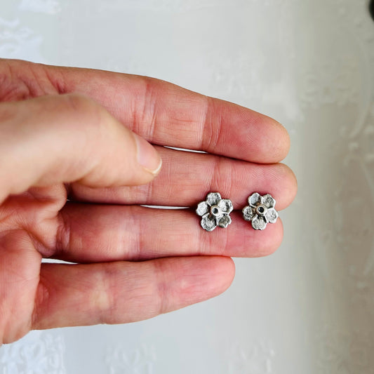 Silver flower-shaped earrings held between fingers against a white background