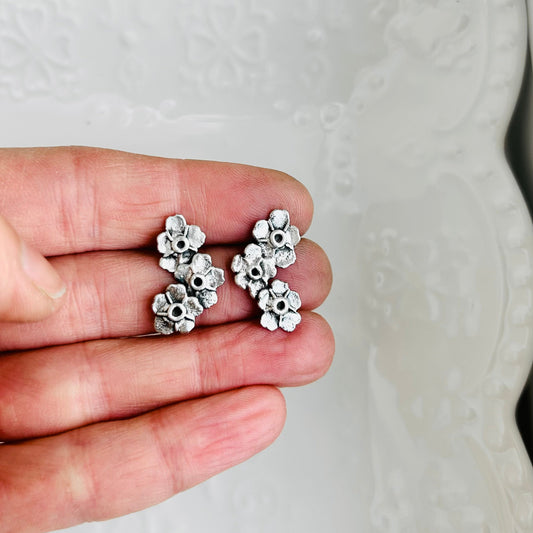Silver floral earrings held between fingers against a textured white background