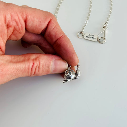 Hand holding a silver pendant with a plain background