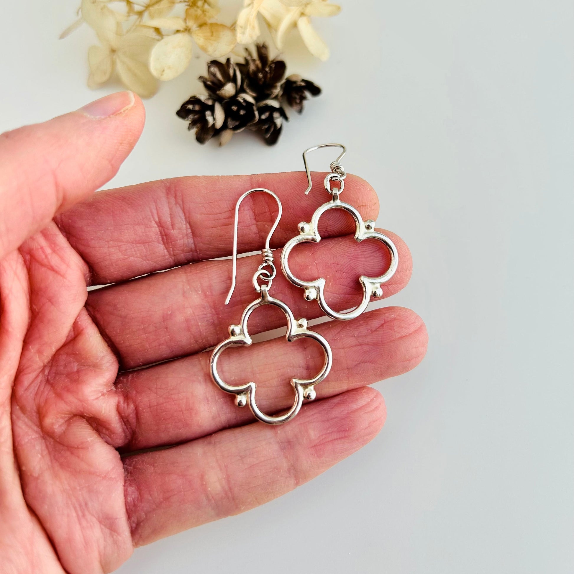 Silver quatrefoil earrings held in a hand with a light background