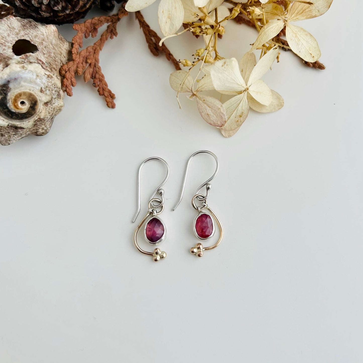 Pair of earrings with pink gemstones on a light gray background with decorative elements.
